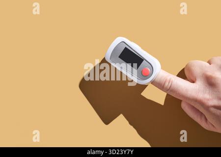 Adult hand using fingertip pulse oximeter on finger against plain background Stock Photo