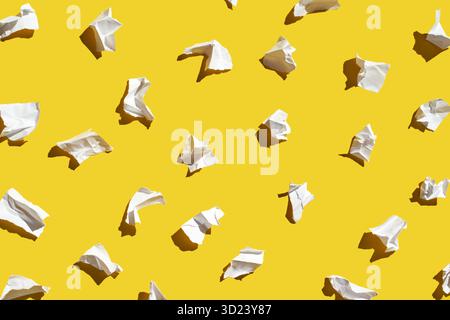Crumpled paper balls on vibrant yellow background in random pattern Stock Photo