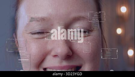 Smiling woman displaying freckles on face in studio workspace, with floating code panels Stock Photo