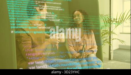 Two software professionals discussing code overlay on sofa in office lounge, with mug and tablet Stock Photo