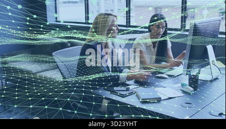 Reviewing documents two colleagues in blazers using computer in office, with network overlay Stock Photo