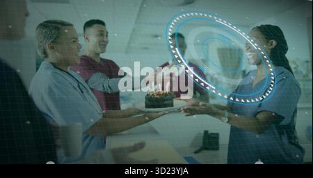 Scrub-clad team passing chocolate cake with lit candles on plate in hospital corridor, celebrating Stock Photo