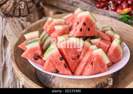 Sliced watermelon triangles on white plate with seeds displayed on wooden table Stock Photo