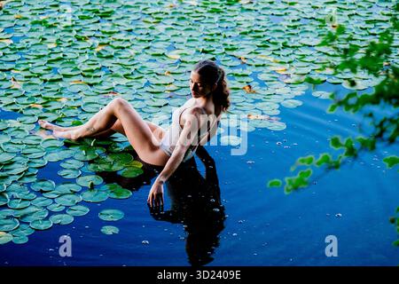 Woman in swimsuit sitting among lily pads on tranquil blue water. Wildcat Lake Park, WA, USA Stock Photo