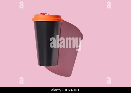 Black coffee cup with orange lid casting shadow on pink background Stock Photo