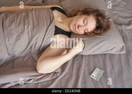 Young caucasian female sleeping peacefully in bed with an empty medicine blister Stock Photo