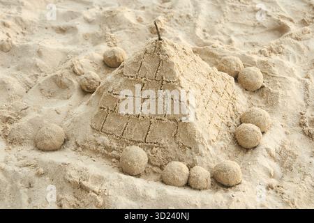 Sand pyramid on beach surrounded by spherical sand sculptures in sunlit setting Stock Photo
