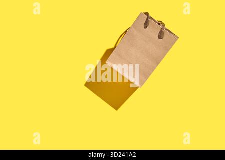 Brown paper shopping bag with handles on vibrant yellow background with shadow Stock Photo