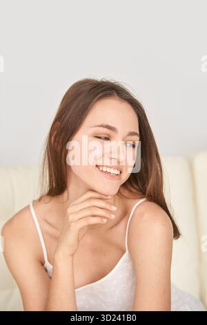 Young caucasian female smiling in white top with hand on chin, relaxed pose Stock Photo