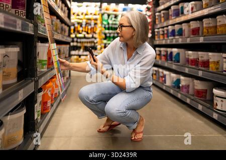 Woman selecting paint color in a home improvement store while crouching down and comparing swatches Stock Photo