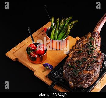 Juicy tomahawk steak served with grilled tomatoes and asparagus on wooden board Stock Photo