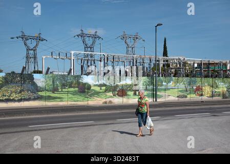 Woman or Electricity Consummer Walks Past an Electricity Substation or Switchyard with Decorated or Painted Security Fence Cavaillon France Stock Photo