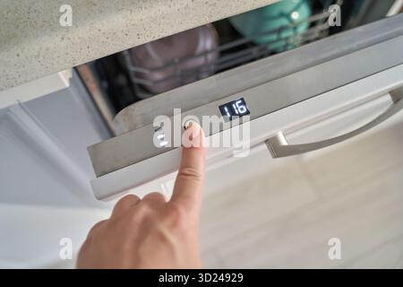 Female hand pressing button on modern dishwasher control panel in kitchen Stock Photo