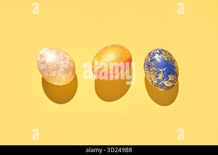 Three colorful decorative eggs on yellow background with shadows celebrating Stock Photo