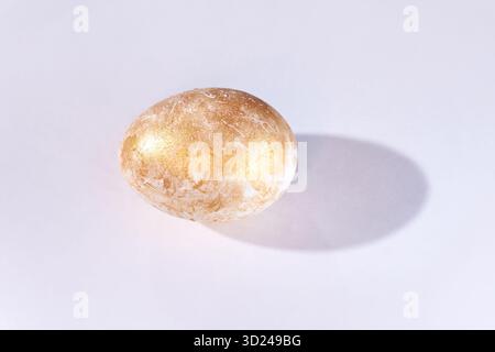 Golden egg on white surface with shadow and subtle texture in minimalist Stock Photo