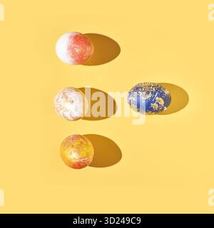 Four colorfully painted easter eggs on yellow background with shadows in artful Stock Photo