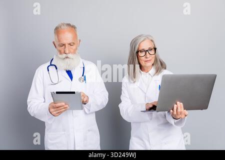 Two experienced doctors review patient information using tablet and laptop in a modern clinic setting Stock Photo
