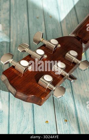Back side of an acoustic guitar headstock showing chrome tuning pegs and wooden texture under natural light on turquoise background. Stock Photo