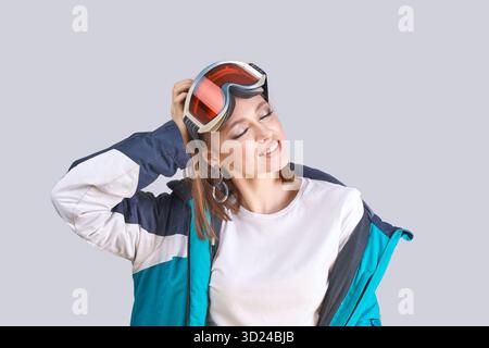Young caucasian female wearing ski jacket and goggles in relaxed pose on gray Stock Photo