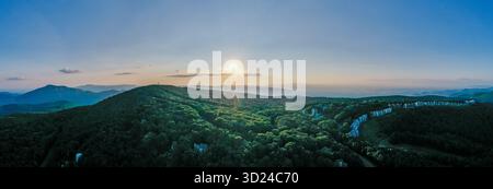Aerial view of a sun-kissed mountain ridge covered in lush green trees, with a distant row of houses nestled among the foliage, Rileyville, Virginia, Stock Photo