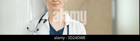 Header of unrecognizable female doctor standing with stethoscope around neck, facing camera with neutral expression, medical professional posing in clinical environment Stock Photo