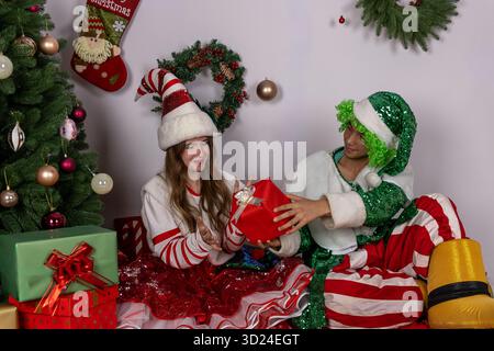 Couple in Santa costumes opening Christmas presents under tree Stock Photo