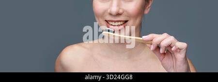 Smiling caucasian female brushing teeth with eco-friendly bamboo toothbrush Stock Photo
