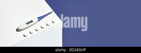Digital thermometer and white pills on minimalist surface against blue Stock Photo