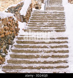 Snow-covered stone steps leading upward with rustic brick walls in winter Stock Photo