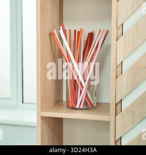 Colorful drinking straws in glass on wooden shelf near window in bright room Stock Photo