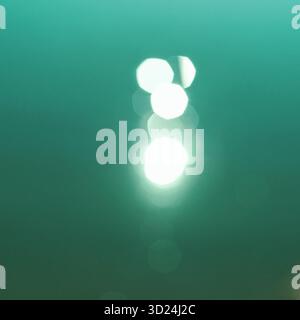 Abstract bokeh light reflections in teal water surface with soft glow effects Stock Photo