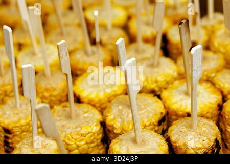 Close-up view of many grilled corn pieces on wooden sticks arranged in rows for serving. Stock Photo