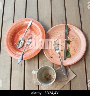 Empty plates and coffee cup on wooden table after meal with cutlery and napkin Stock Photo