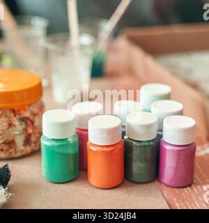 Colorful variety of craft paint bottles on table with glitter and brushes Stock Photo