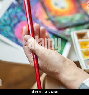 Female artists hand holding red brush with colorful paintings and watercolor Stock Photo