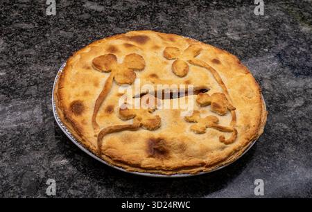 Home made apple pie, decorated crust of rough puff pastry, on a granite work surfasce counter top Stock Photo