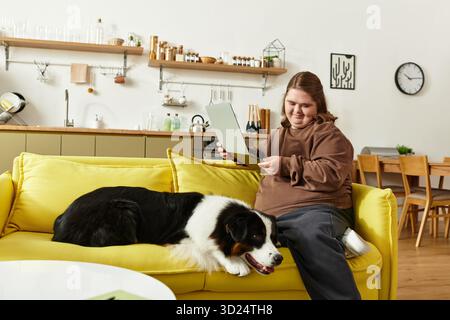 A young woman with Down syndrome relaxes on a yellow couch, reading with her dog. Stock Photo