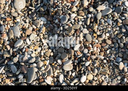 A detailed close-up of small, rounded stones and pebbles in varied colors, creating a rich, textured surface. Ideal for themes of nature, beach textures, geology, and calm, organic design. Stock Photo