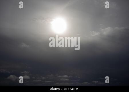 View of a large hazy sun shining dimly through layers of overcast cloud Stock Photo