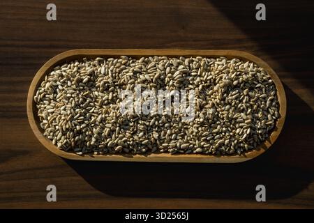 Sunflower seeds in wooden bowl on dark wooden background under warm natural light. Stock Photo