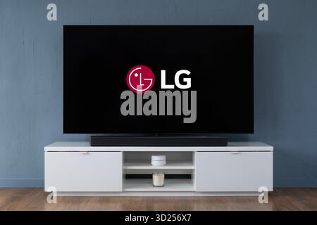 A 2025 LG OLED widescreen television is seen sat upon a white cabinet in a contemporary living room. Stock Photo