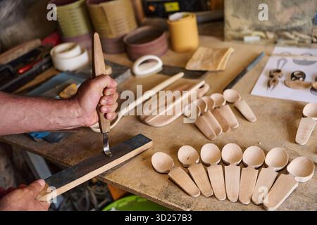 Handcrafting wooden spoons, a craftsman carving wood with a gouge, handmade wooden kitchenware, traditional wood carving tools on a workbench, artisan Stock Photo