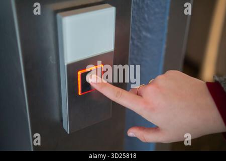 Finger pressing illuminated red button near door for access or communication system. Stock Photo