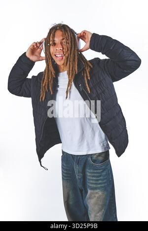 Smiling young man with dreadlocks enjoying audio, wearing headphones and a black jacket Stock Photo