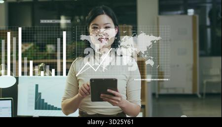 Data analyst woman wearing beige and brown outfit reviewing 3D charts at office desk, with tablet Stock Photo