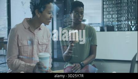 Collaborating two tech coworkers reviewing code on laptop at modern office lounge, with coffee cups Stock Photo