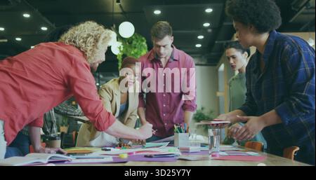 Collaborating colleagues reviewing sketches on wooden table in office, with pens and markers Stock Photo