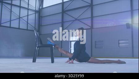 Performing split stretch athlete in sportswear on gym floor, with black plastic chair, copy space Stock Photo