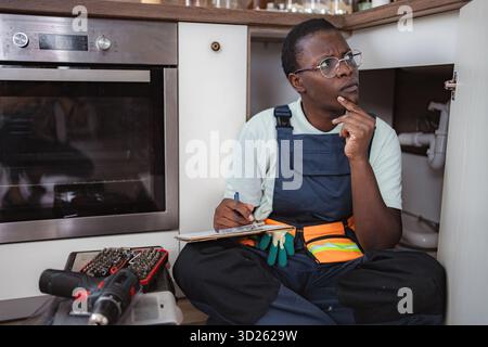 Plumber inspecting pipes and taking notes in kitchen Stock Photo