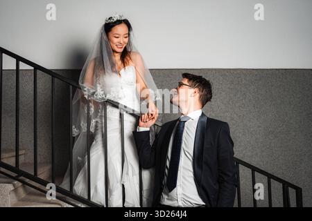 Interracial couple holding hands on stairs after wedding Stock Photo